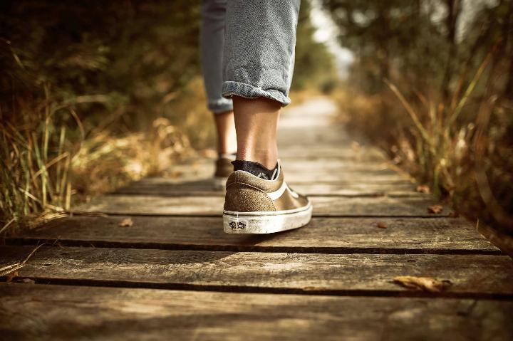 Een persoon die een wandeling maakt met MijnBeweegcoach op een houten pad.